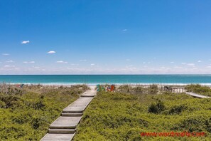 A wooden boardwalk leading to a beach with clear blue water and a clear sky.