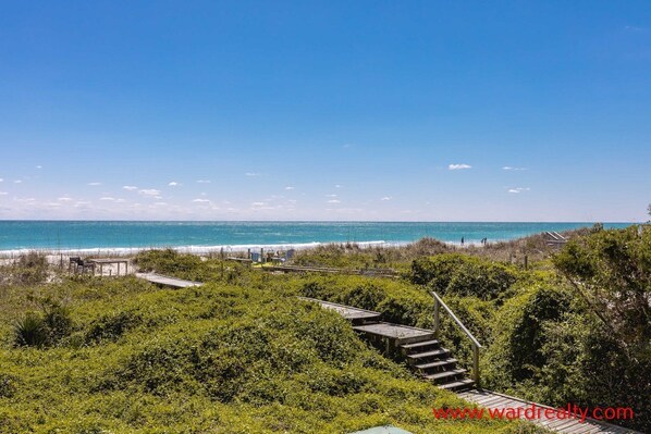 A coastal view with a wooden staircase leading to a beach area, surrounded by greenery.
