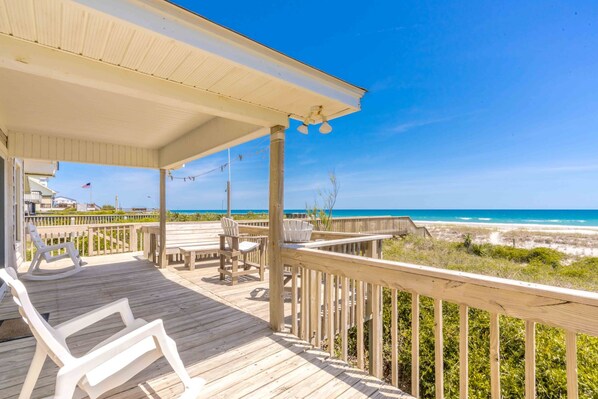 A wooden deck with chairs and a table, overlooking a beach with a clear sky.