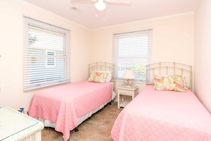 A bedroom with two beds, each with a pink bedspread and matching pillows, a small bedside table with a lamp, and a ceiling fan. - Summer Girl - Oceanfront! 4 Bedroom Cottage (Topsail Beach)