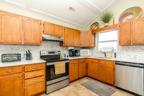 A kitchen with wooden cabinets, a stainless steel oven, a microwave, and a dishwasher. - Summer Girl - Oceanfront! 4 Bedroom Cottage (Topsail Beach)