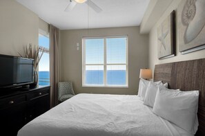 Une chambre d’hôtel avec un grand lit, un téléviseur posé sur une commode, une fenêtre avec des stores et des œuvres d’art accrochées au mur.