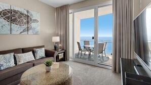 Ett hotellrum med en soffa, ett soffbord, en TV, en takfläkt, en tavla och en balkong med utsikt över havet.