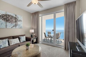 Une chambre d’hôtel équipée d’un canapé, d’une table basse, d’une télévision, d’un ventilateur de plafond, d’un tableau et d’un balcon avec vue sur l’océan.