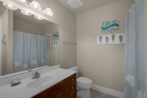 Un baño con lavamanos blanco, un espejo, inodoro y cortina de ducha. Hay un letrero en la pared que dice 'Life is better in flip flops'.