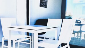 Een moderne kamer met een witte tafel en stoelen, een zwarte bank en een gekaderd schilderij aan de muur.