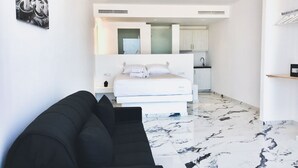Een moderne hotelkamer met een bed, een zwarte bank, een marmeren vloer, een keukenhoek en een badkamer.