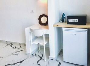 Kitchenette with refrigerator, microwave, and chair, featuring a round mirror above the counter.