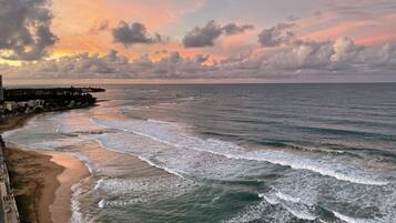 A coastal view with waves, a beach, and a distant shoreline with buildings.