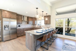 A modern kitchen with a central island, stainless steel appliances, and large windows.