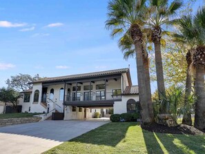 A two-story house with a covered patio, palm trees, and a well-maintained lawn.
