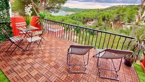 A wooden deck with outdoor furniture, a railing, and a view of a green landscape and water. - Casa Rural La Goleta.  Pantano de San Juan (San Martín de Valdeiglesias)