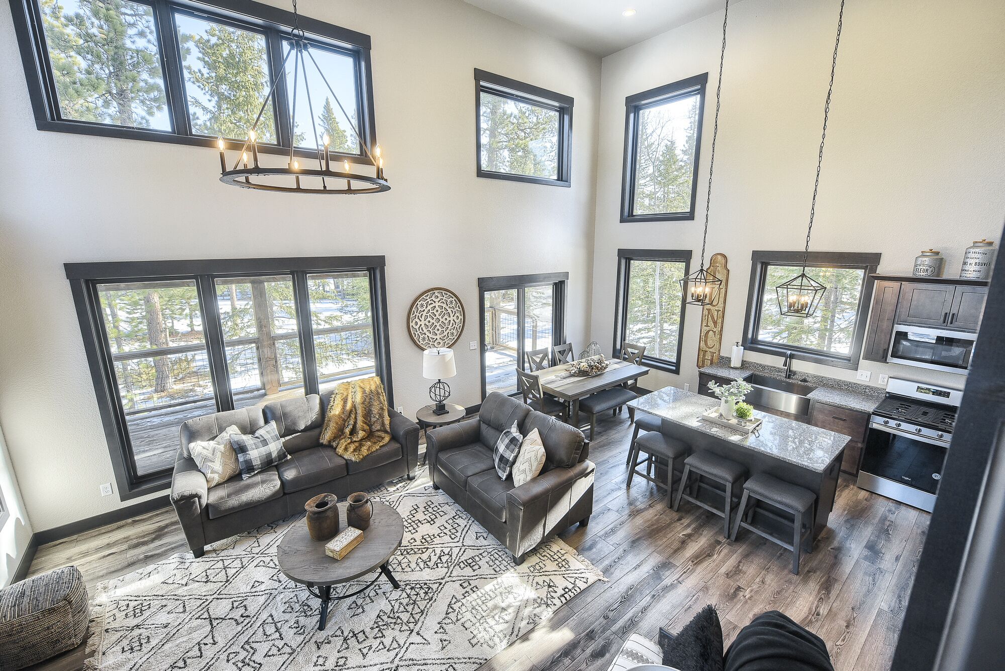 A spacious living area with a large window, a fireplace, and a dining area with a kitchen in the background.
