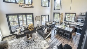 A spacious living area with a large window, a fireplace, and a dining area with a kitchen in the background.