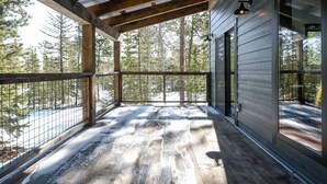 A wooden deck with metal railings overlooking a snowy forest.