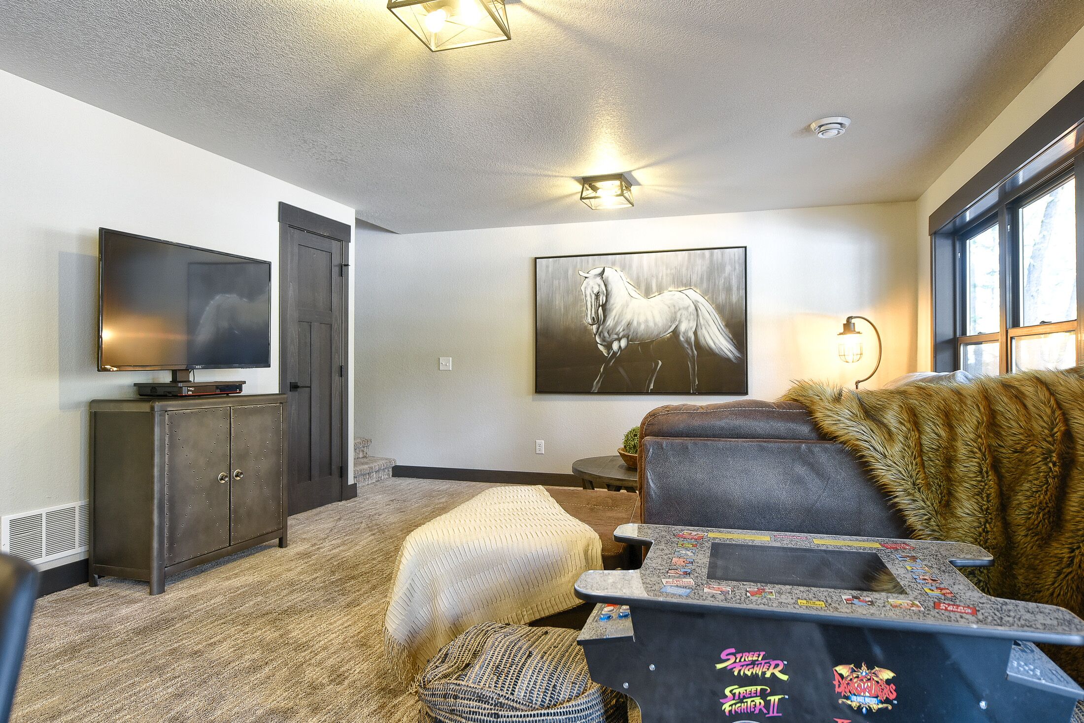 A modern living room with a flat-screen TV, a mounted painting, and a cozy seating area with a fur throw.