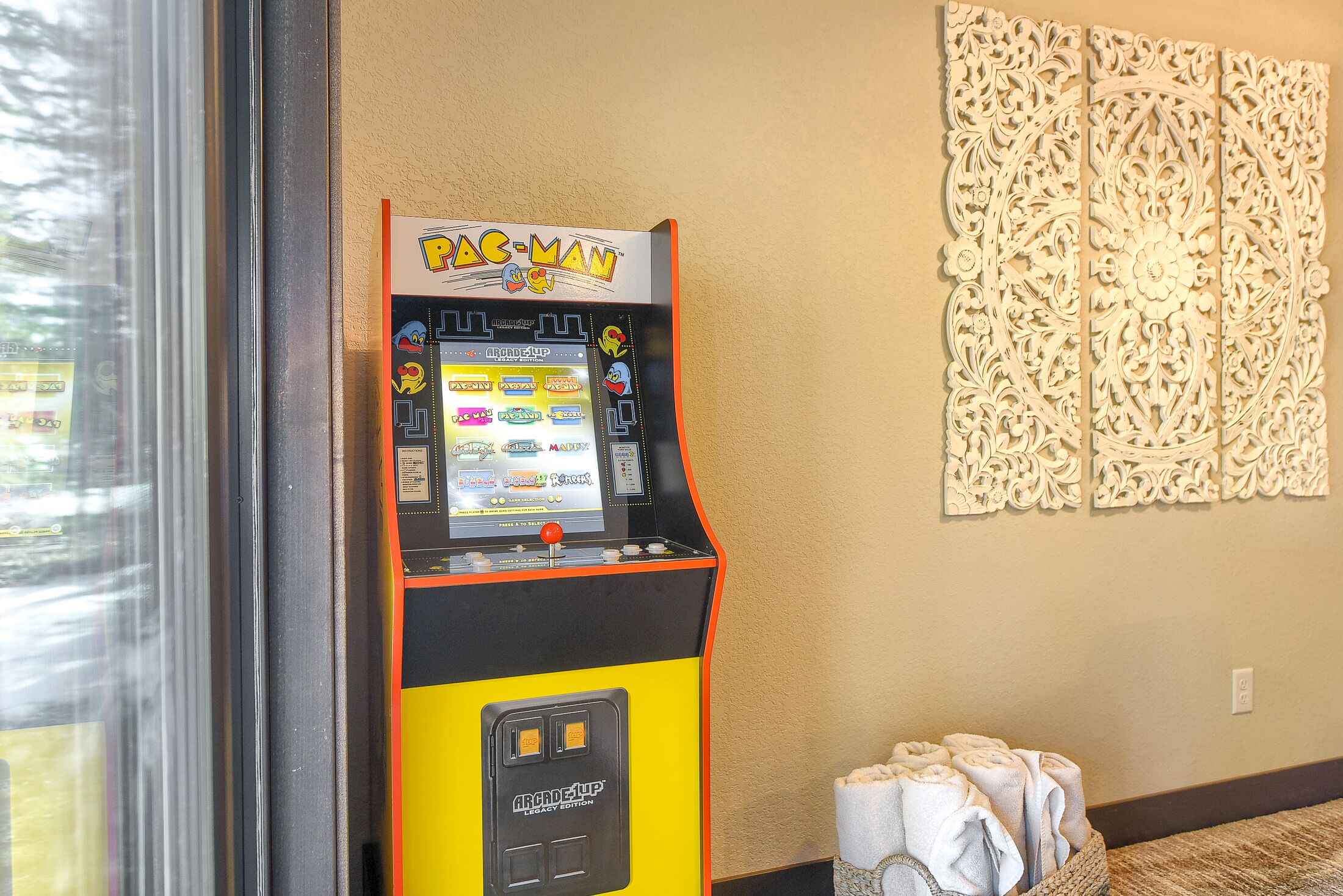 En Pac-Man-spelautomat i ett rum med en dekorativ väggpanel och handdukar på golvet.