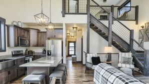 A spacious kitchen with a central island, wooden flooring, and a staircase leading to an upper level.