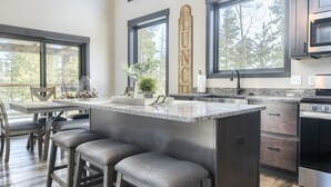 A modern kitchen with a large island, bar stools, and a view of the outdoors through large windows.