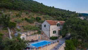 A stone house with a swimming pool, surrounded by greenery and hills. - Villa Dol (Postira)