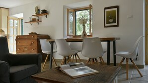 A dining area with a wooden table, white chairs, a wooden cabinet, and a window with a view of trees. - Villa Dol (Postira)