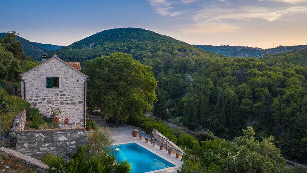 A stone building with a pool, surrounded by lush greenery and hills. - Villa Dol (Postira)