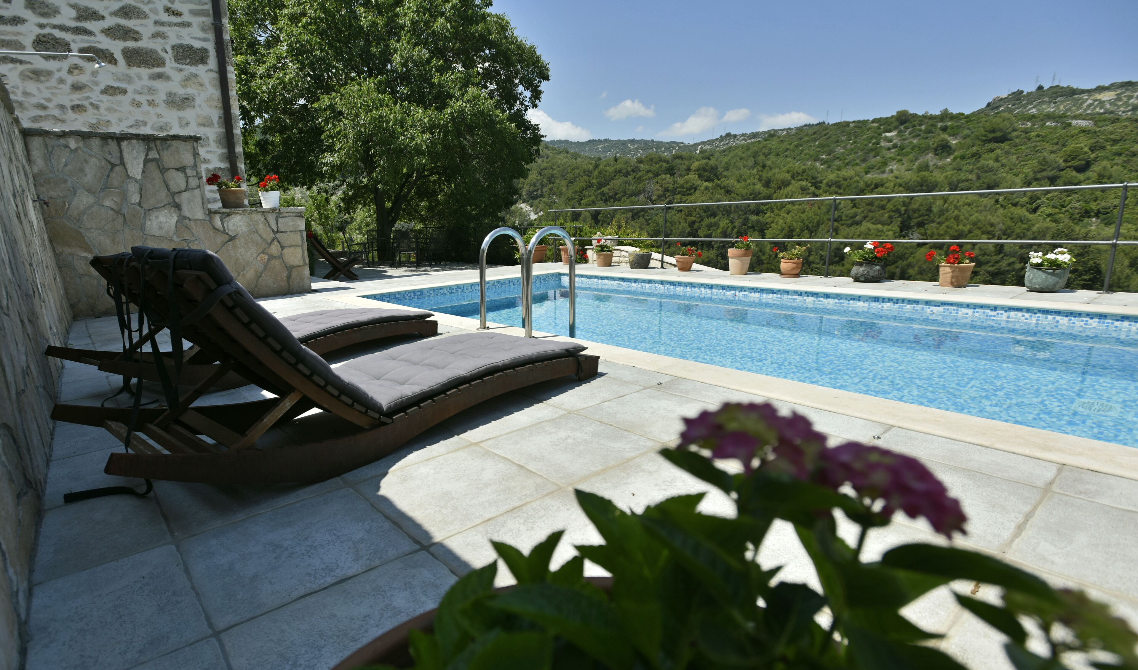 A pool with two lounge chairs and a stone wall.