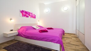 A modern bedroom with a white bed, pink bedding, and a wooden floor. - Orchid Spadici / Apartment Orchid Spadici (Porec)