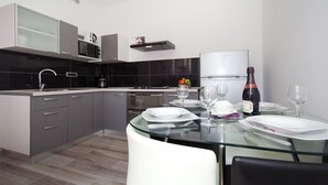 A modern kitchen with a glass dining table set for two, a microwave, a coffee maker, and a wine bottle. - Orchid Spadici / Apartment Orchid Spadici (Porec)
