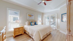 Une chambre avec un grand lit, deux tables de chevet, un ventilateur de plafond et une vue sur l’extérieur, visible à travers la porte.