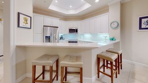 Une cuisine moderne avec des meubles blancs, un réfrigérateur en acier inoxydable, un four à micro-ondes et un grand îlot central doté de tabourets.