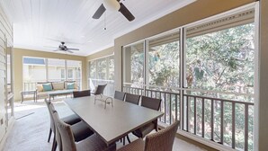 Une terrasse couverte avec une table et des chaises, de grandes fenêtres et un ventilateur de plafond.
