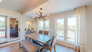 A spacious dining area with a wooden table, cushioned benches, and a modern chandelier. - Completely Updated Two Bedroom Condominium with Sweeping Marina Views! (Hilton Head)