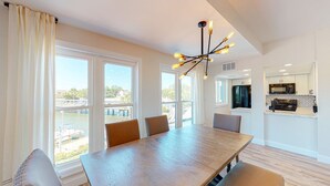A spacious dining area with a large wooden table and chairs, a modern chandelier, and large windows offering a view of the outdoors. - Completely Updated Two Bedroom Condominium with Sweeping Marina Views! (Hilton Head)