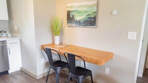 A small kitchen with a wooden table and two chairs, a potted plant, and a painting on the wall.