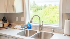 A modern kitchen with two stainless steel sinks, a window with a view of greenery, and white cabinetry.