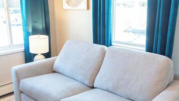 A light grey sofa in a room with a large window, blue curtains, and a framed artwork on the wall.