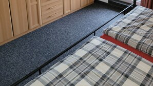 Un dormitori amb un armari ampli, un llit amb roba de llit escocesa, un mirall i una finestra amb cortines.