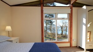 Une chambre à coucher comprenant un lit, une table de chevet, une commode et une fenêtre donnant sur des arbres et une route.