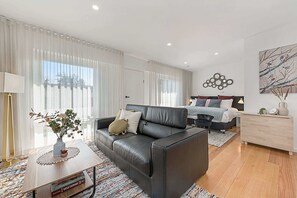 A modern living room with a black leather sofa, a wooden coffee table, and a dining area with a white table and chairs.