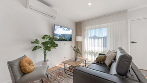 A modern living room with a sofa, a chair, a coffee table, and a large window with sheer curtains. - Comfy Studio with Shared Backyard near Racecourse (Carnegie)
