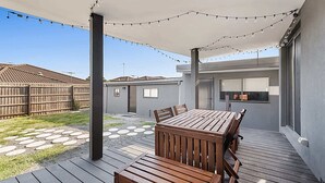 A patio with a wooden table and chairs, a string of lights, and a covered area with a view of neighboring houses. - Gorgeous 3-Bed House with Spacious Shared Backyard (Carnegie)