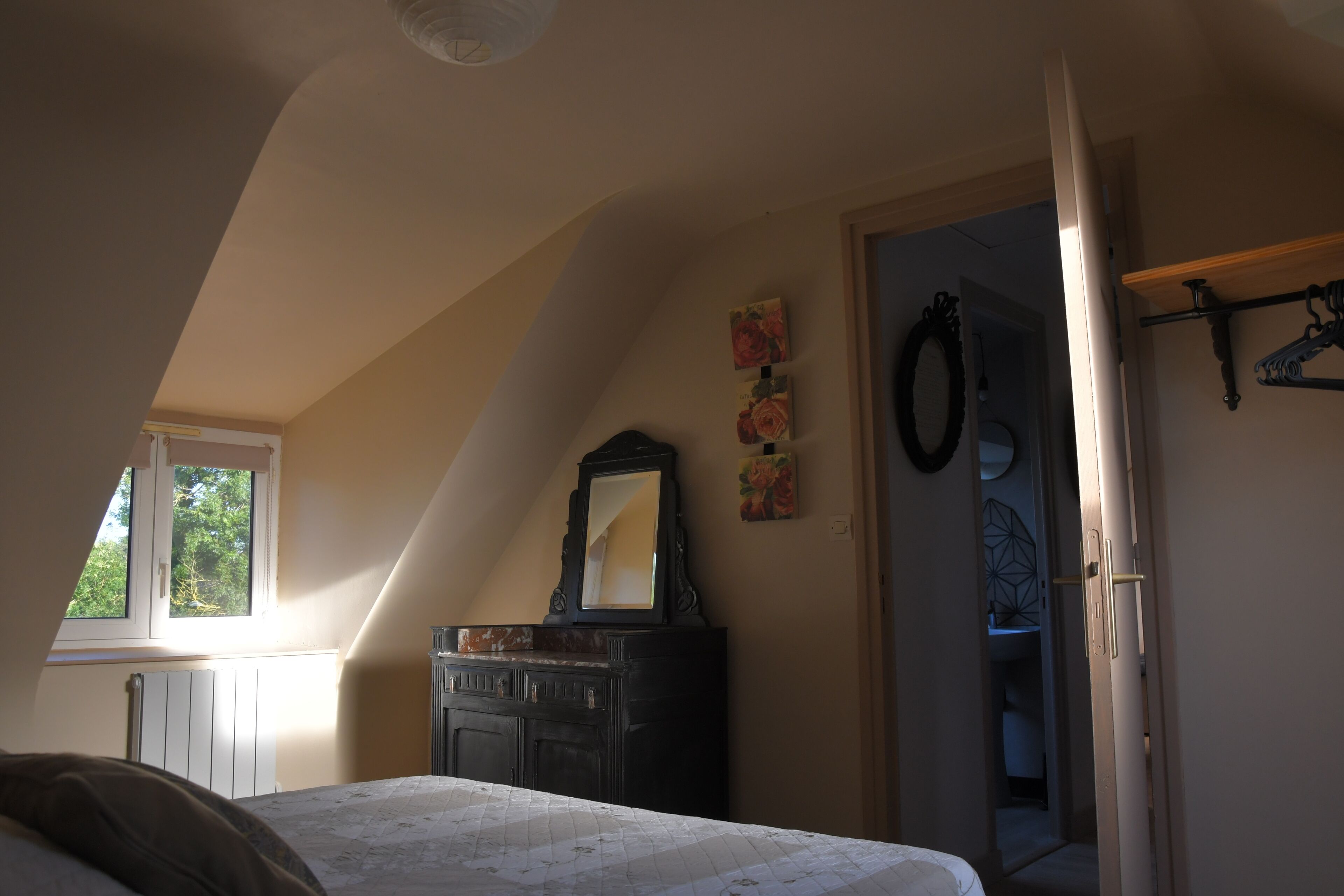 Ein Schlafzimmer mit Schräge, einem Bett, einer Kommode, einem Spiegel und einem Fenster.