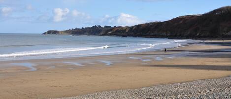 A pebbly beach with a rocky shoreline and a distant view of a hill.