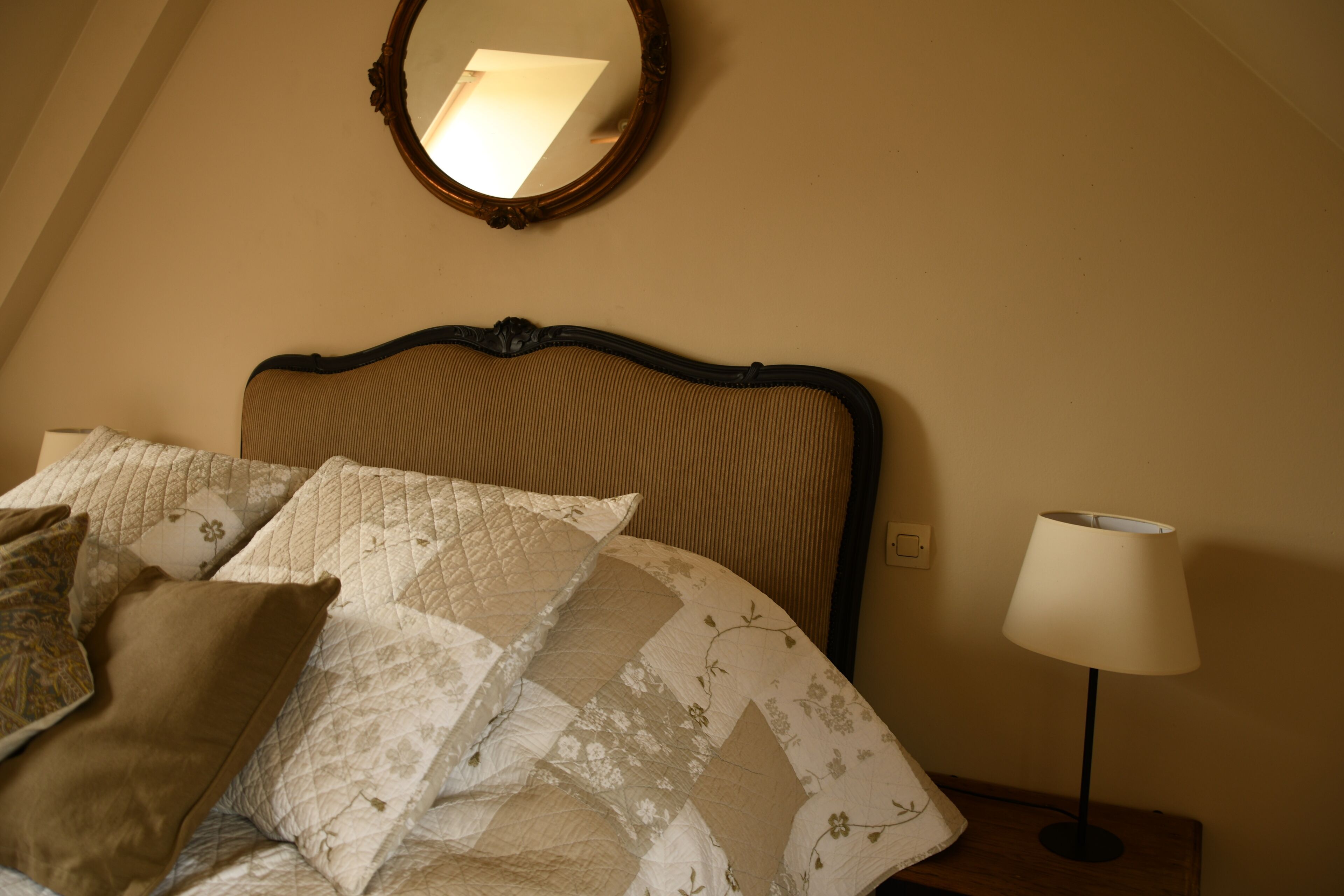 A neatly made bed with a quilt, a bedside lamp, and a mirror on the wall.
