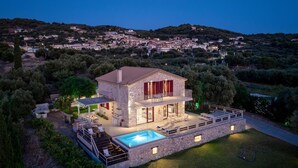 A stone house with a swimming pool, outdoor seating, and a view of a hillside village. - Arca Villa   Enchanting Sunset! (Keri)