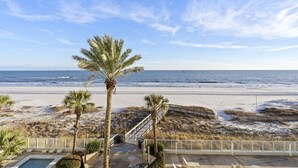 Une vue sur la plage depuis un balcon agrémenté de palmiers, avec une piscine et une terrasse en bois.