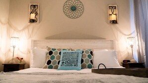 Una camera d'albergo con un letto, due comodini con lampade, applique decorative e un quadro appeso al muro.