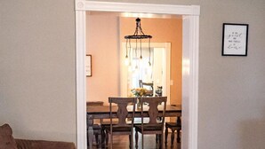 Un soggiorno con un divano marrone, un tavolino in legno e un tappeto. Sullo sfondo, un'area pranzo con un lampadario.