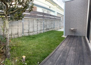 Un jardin avec une terrasse en bois, un mur en béton et une petite table.